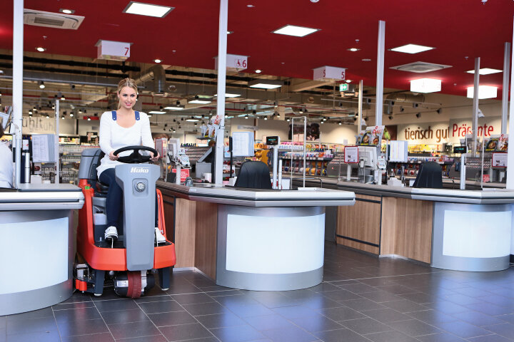 Reinigungspersonal reinigt im engen Kassenbereich mit der Aufsitz-Scheuersaugmaschine B75-R von Stangl